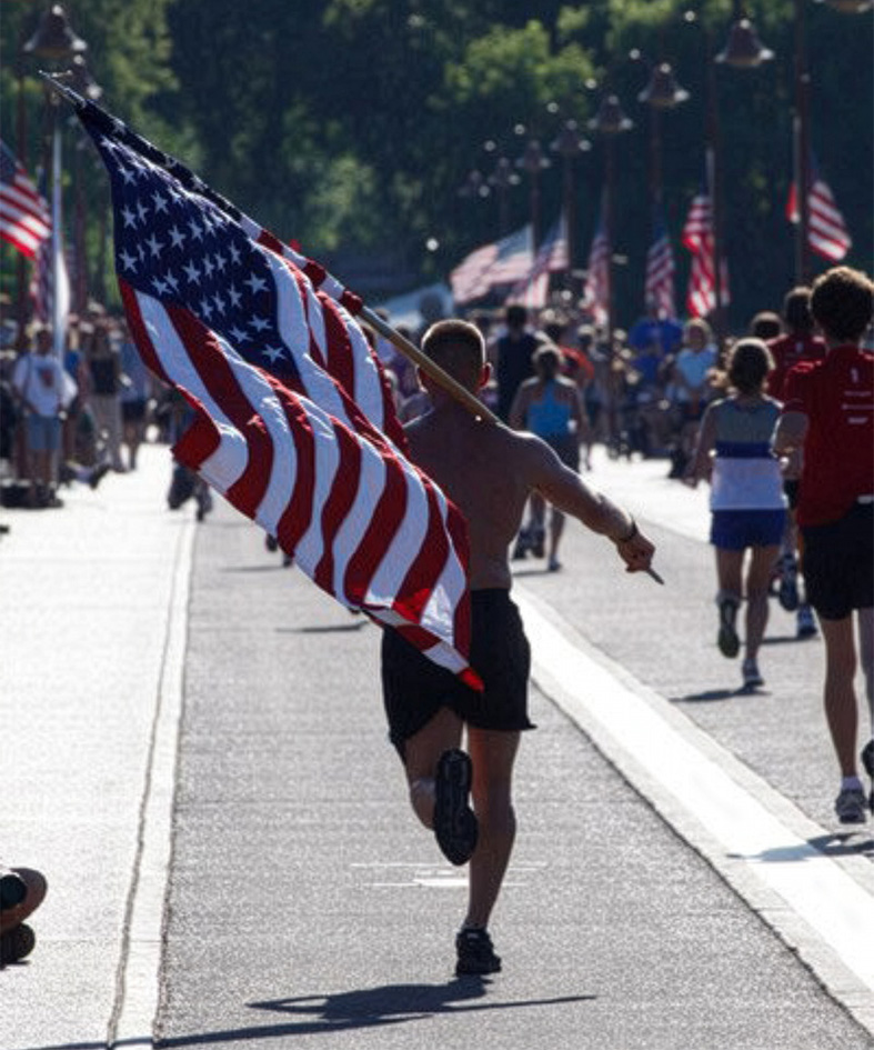 Adam Schwarze running with a large American flag against his shoulder.